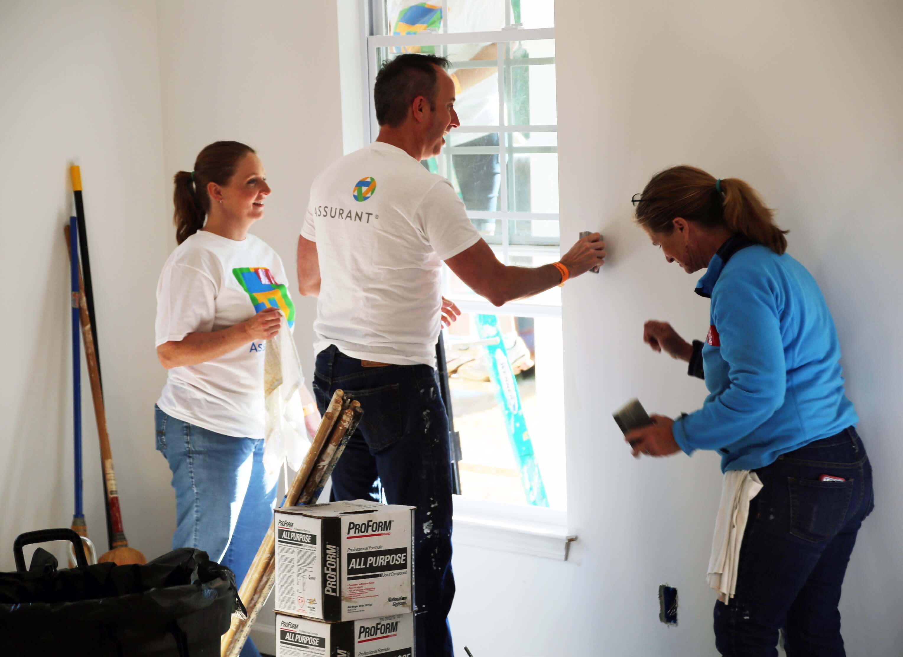 Assurant Workers Three Assurant employees working at a Habitat for Humanity build sanding walls